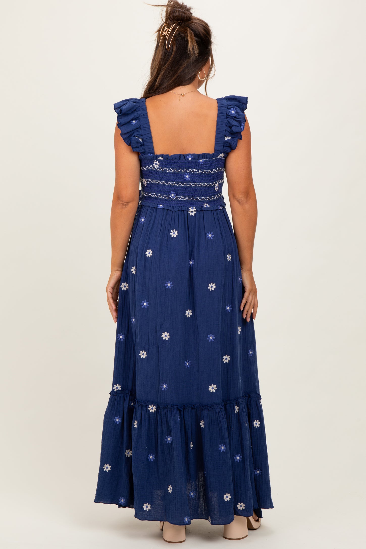 woman wearing a navy blue maternity maxi dress with ruffle sleeves and floral embroidery, showing off her baby bump