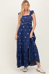 woman wearing a navy blue maxi dress with floral embroidery and ruffled straps, standing in casual white sneakers