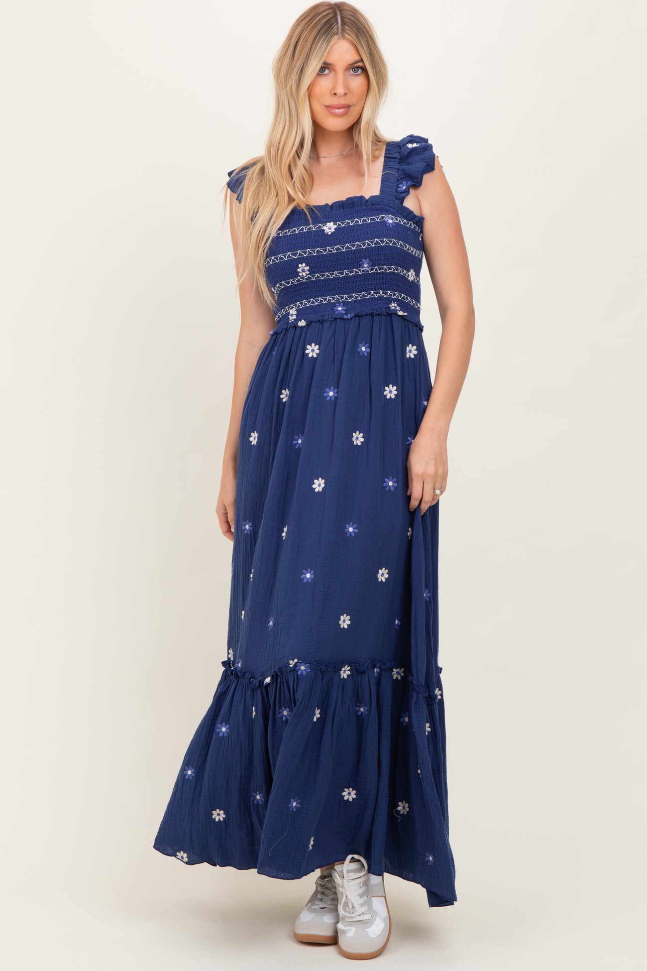 woman wearing a navy blue maxi dress with floral embroidery and ruffled sleeves, styled with white sneakers