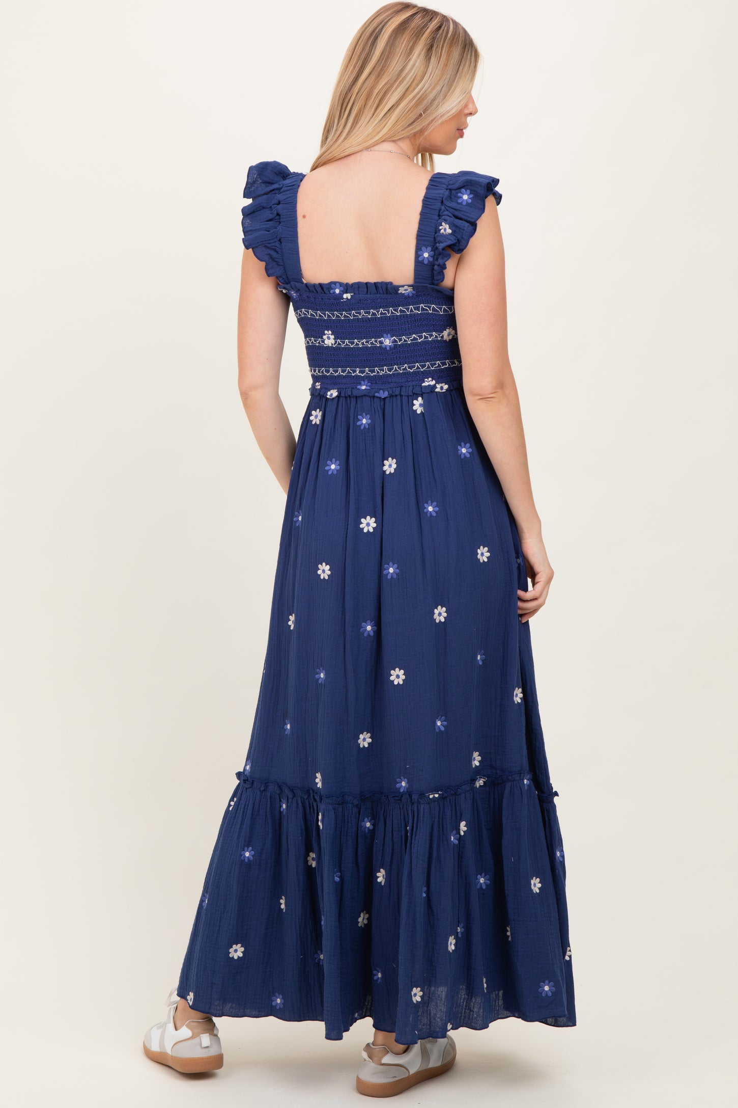 woman wearing a navy blue floral embroidered maxi dress with ruffled sleeves and a smocked bodice, shown from the back