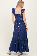 woman wearing a navy blue floral embroidered maxi dress with ruffled sleeves and a smocked bodice, shown from the back