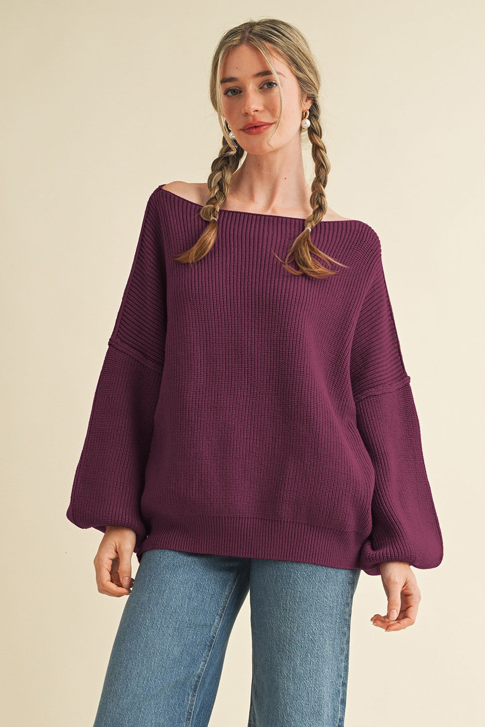 woman wearing a dark purple oversized off-the-shoulder sweater with balloon sleeves and blue jeans