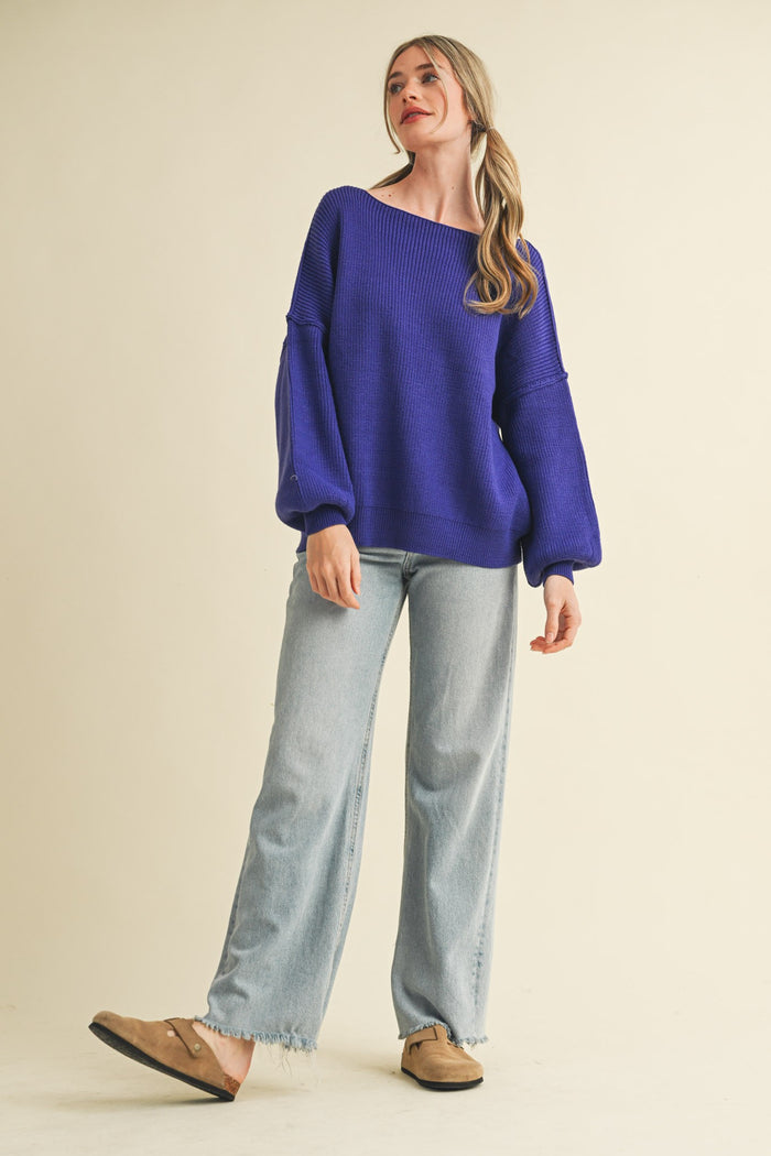 woman wearing a purple oversized sweater and light blue wide-leg jeans, standing against a neutral background