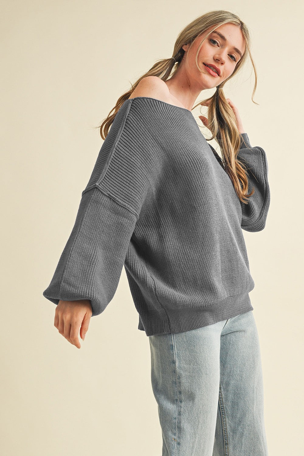 woman wearing a gray off-shoulder oversized sweater with balloon sleeves and light blue jeans