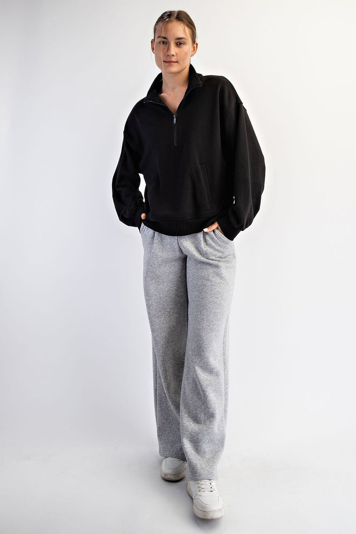 woman wearing a black zip-up sweatshirt and gray wide-leg sweatpants with white sneakers