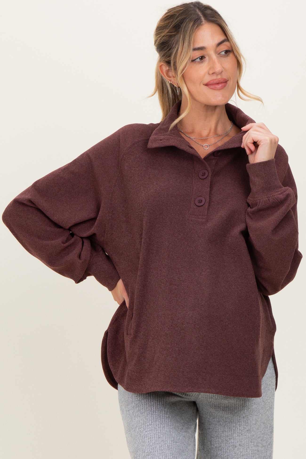 woman wearing a burgundy long sleeve maternity pullover with a collar and button detail, smiling at the camera