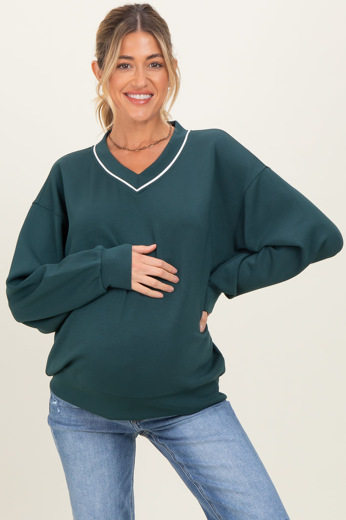 woman wearing a dark green maternity sweatshirt with a v-neck and white detailing, showing her baby bump