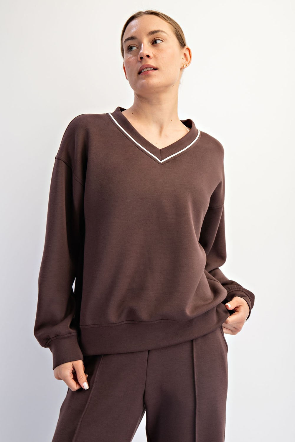 woman wearing a brown v-neck sweatshirt with white detailing and relaxed fit, posing against a white background