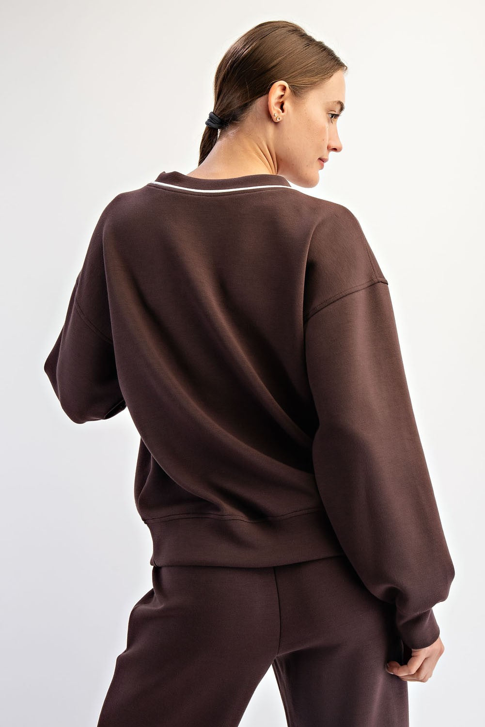 woman wearing a brown oversized sweatshirt with a relaxed fit and white detailing on the neckline, shown from the back