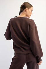 woman wearing a brown oversized sweatshirt with a relaxed fit and white detailing on the neckline, shown from the back