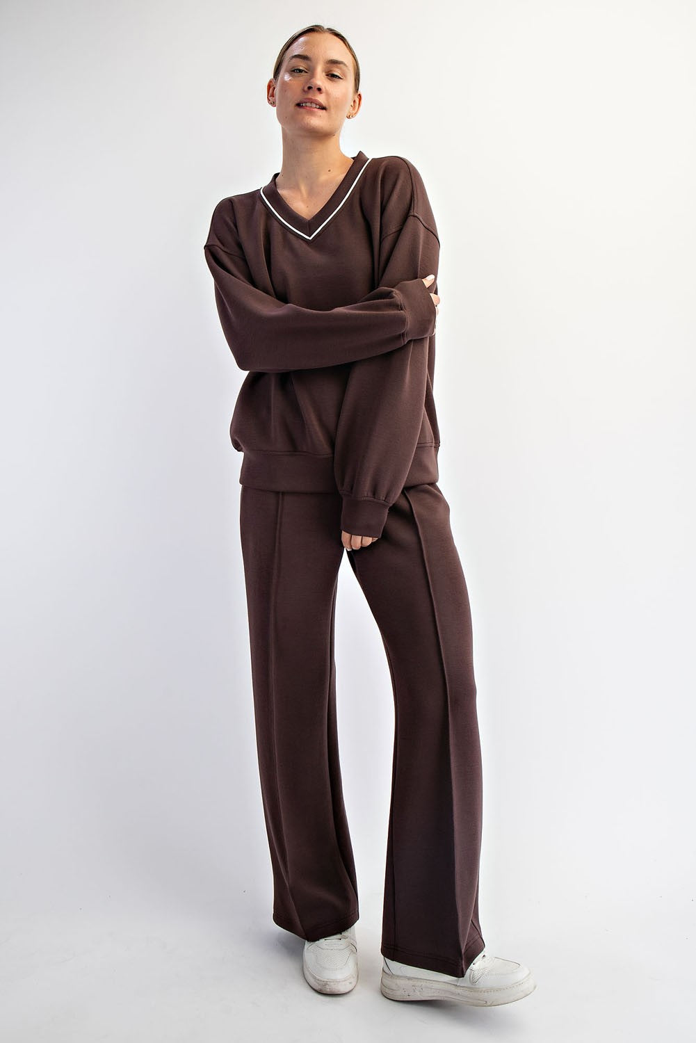 woman wearing a brown v-neck sweatshirt and matching wide-leg pants, styled with white sneakers