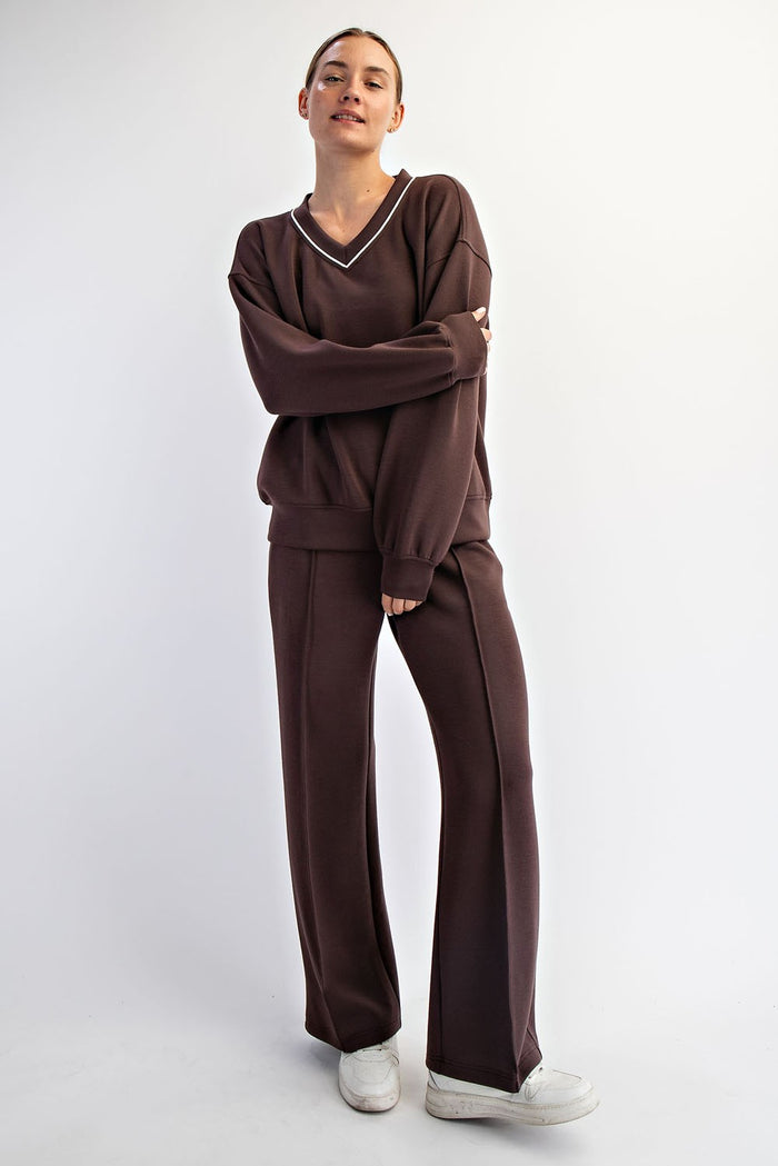 woman wearing a brown v-neck sweatshirt and matching wide-leg pants, styled with white sneakers