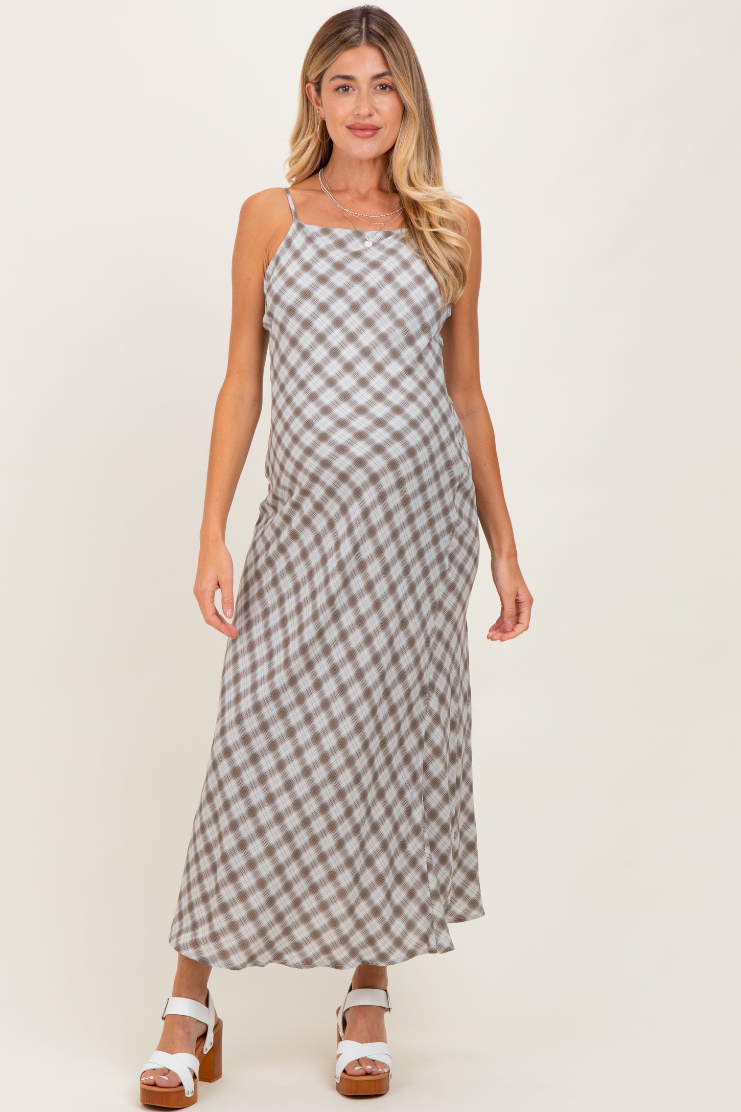 woman wearing a brown and white checkered maternity maxi dress with spaghetti straps and a visible baby bump