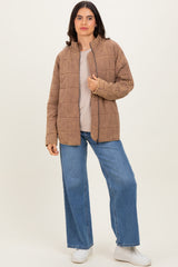 woman wearing a tan quilted jacket over a light top and blue wide-leg jeans, posing against a neutral background
