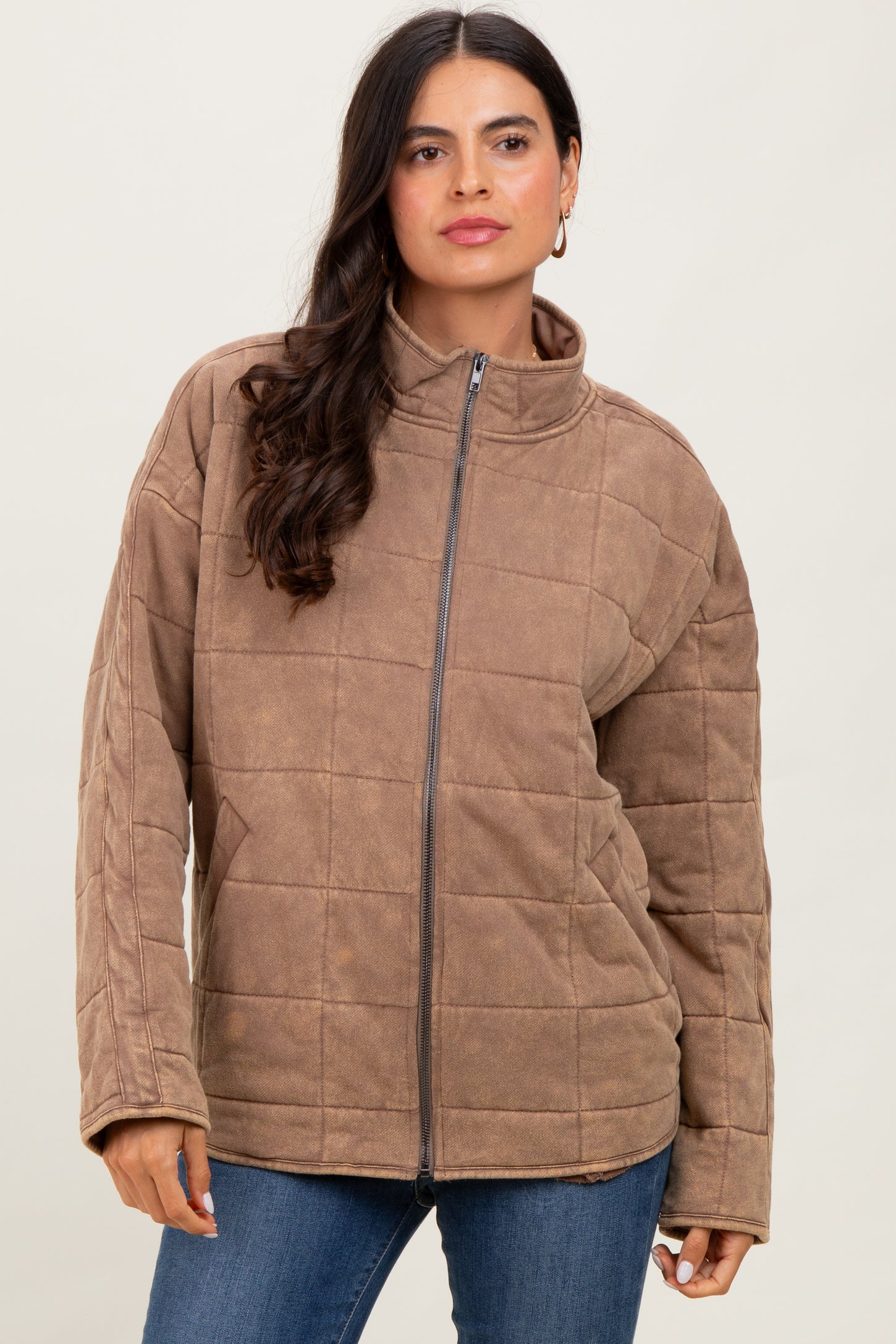 woman wearing a brown quilted zip-up jacket with a high collar and long sleeves, paired with jeans