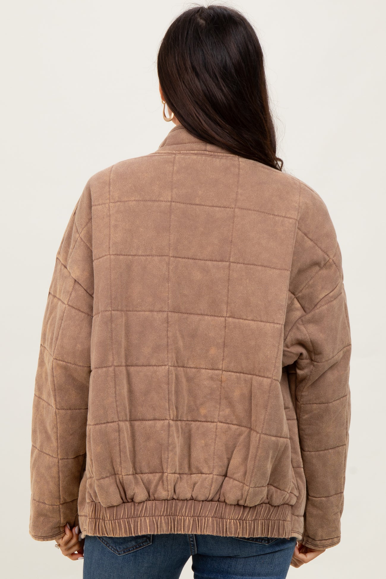 woman wearing a brown quilted jacket with a relaxed fit and elasticized hem, viewed from the back