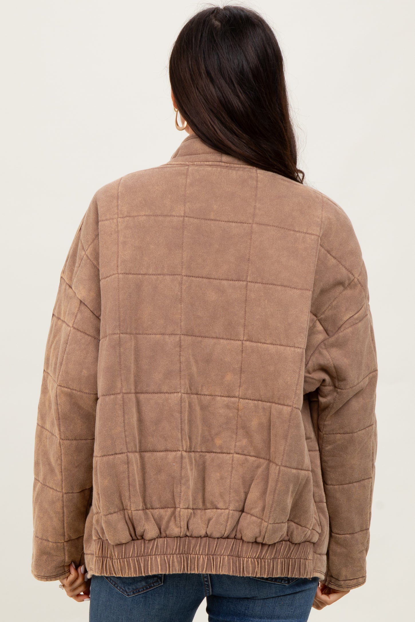 woman wearing a brown quilted jacket with a relaxed fit and elasticized hem, viewed from the back