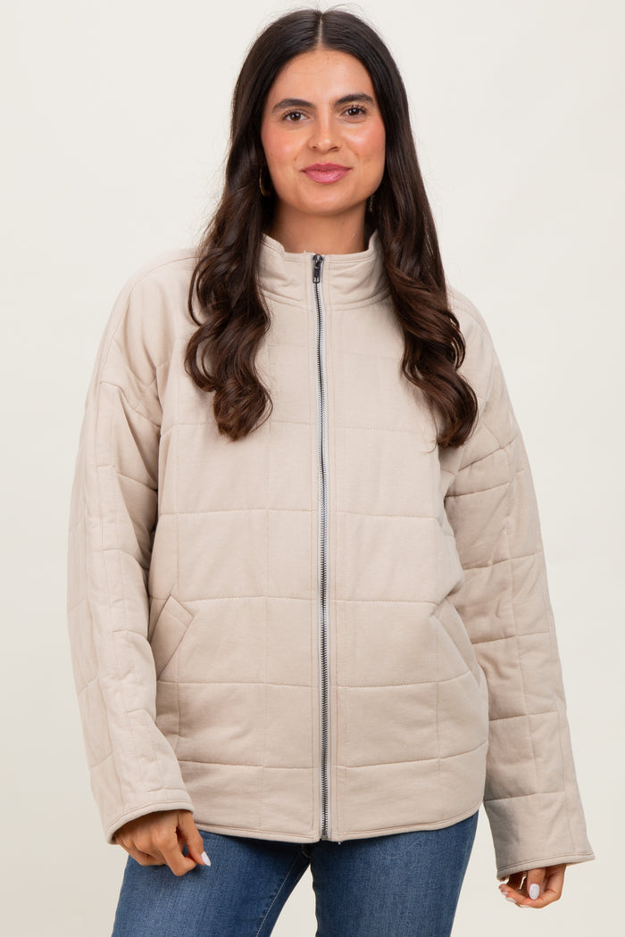woman wearing a tan quilted zip-up jacket with a high collar and blue jeans