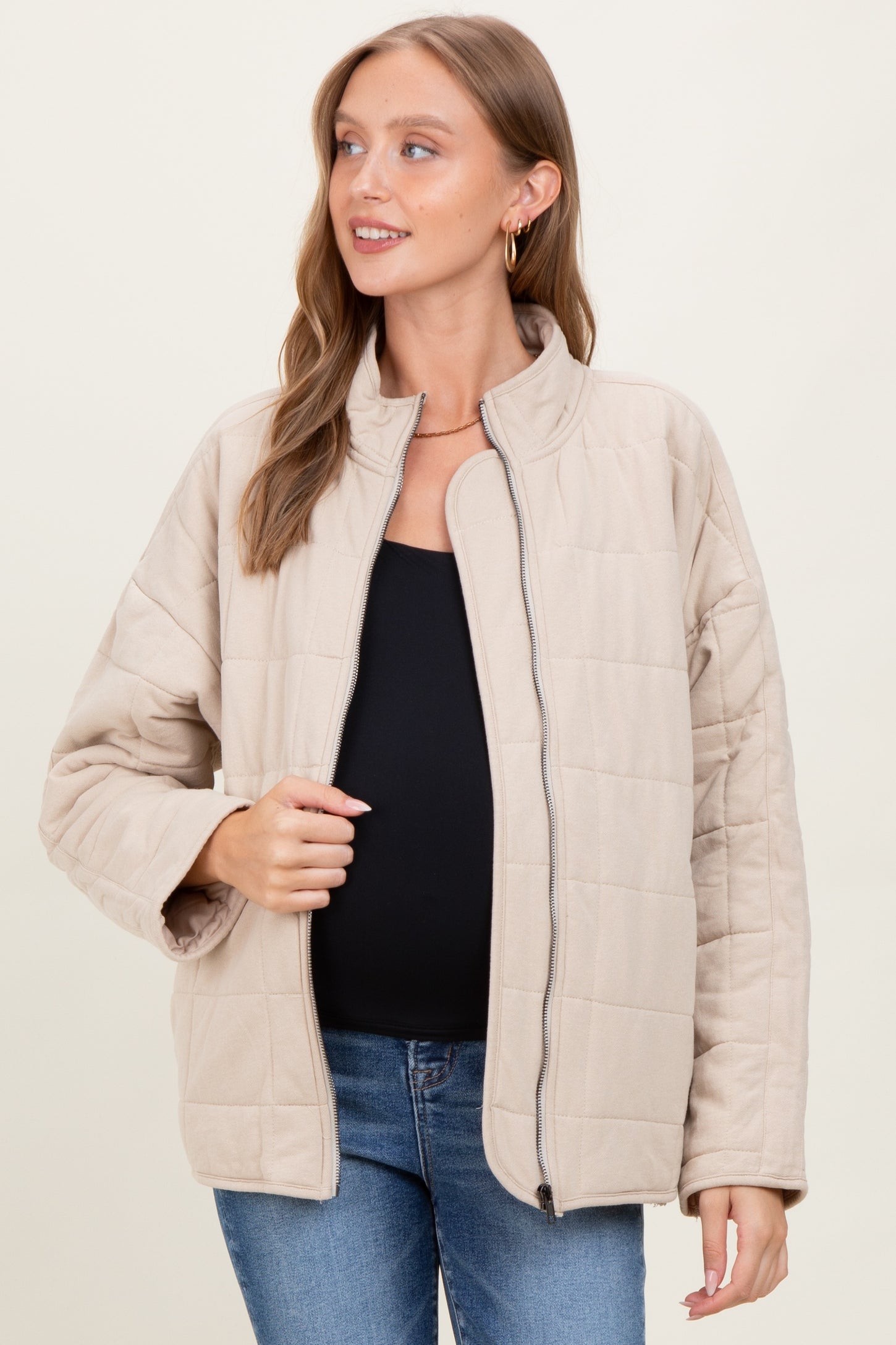 woman wearing a beige quilted maternity jacket over a black top and smiling