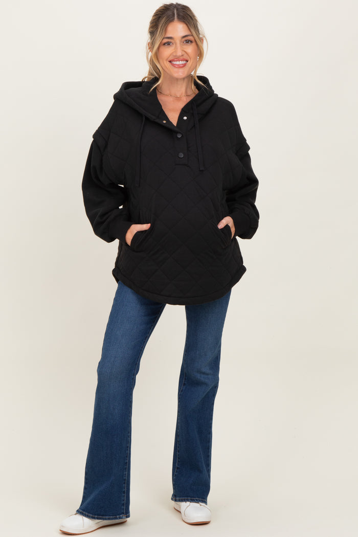 woman wearing a black quilted maternity hoodie with a front pocket and button detail, paired with blue flared jeans