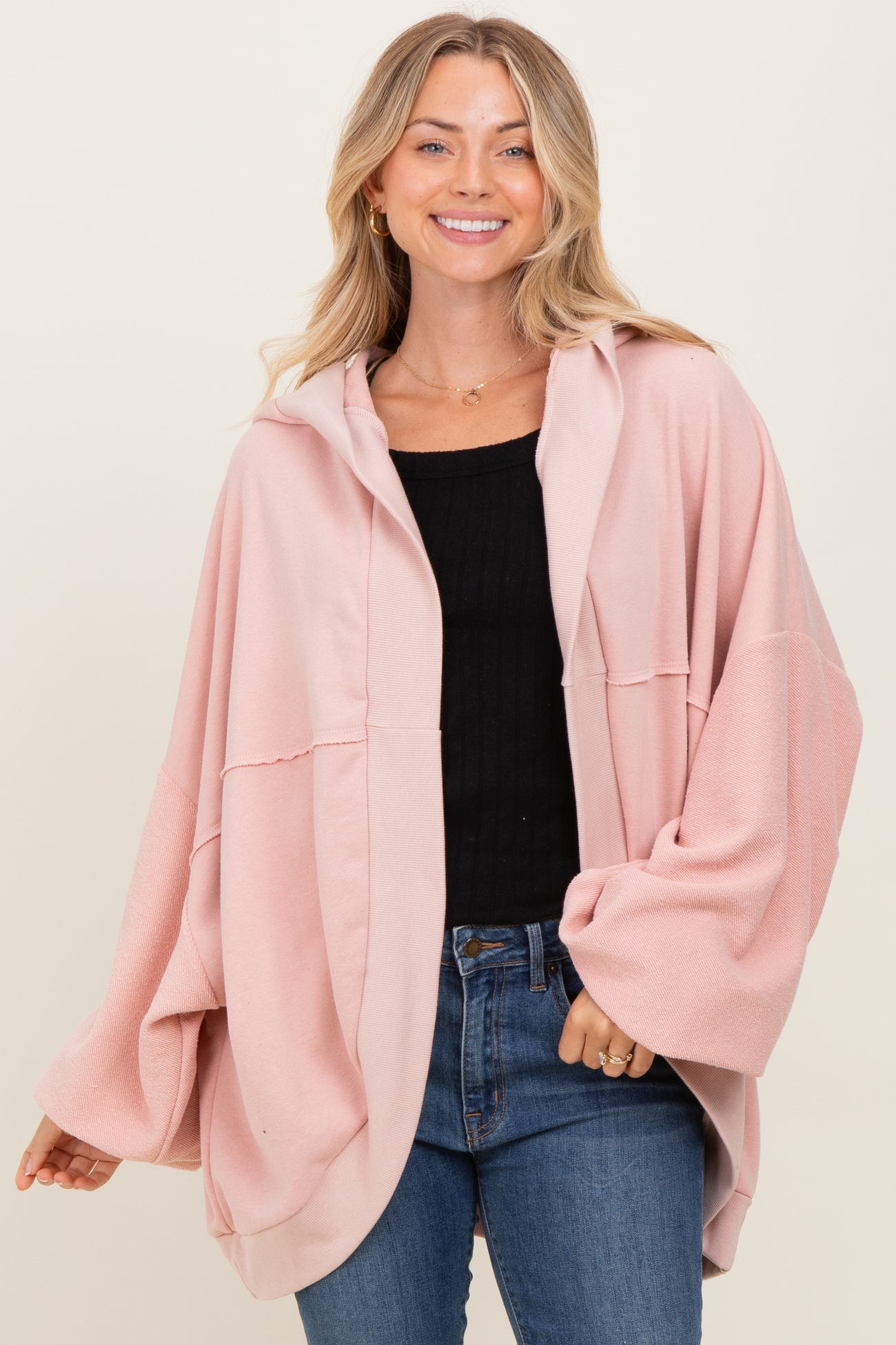 woman wearing a blush pink oversized hoodie with a front button closure and wide sleeves, paired with jeans