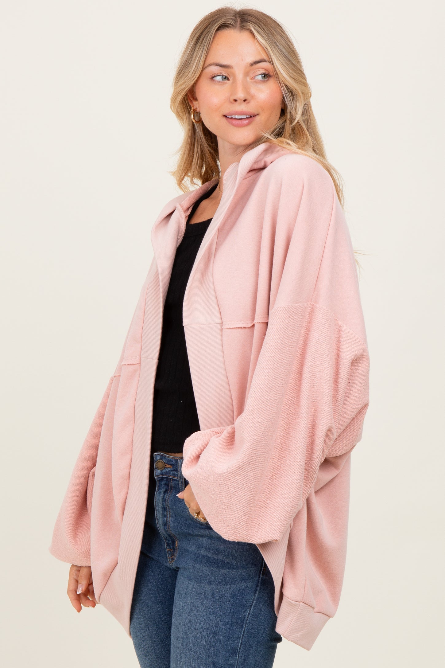 woman wearing a soft pink oversized cardigan with a hood and dropped shoulders, paired with a black top and jeans