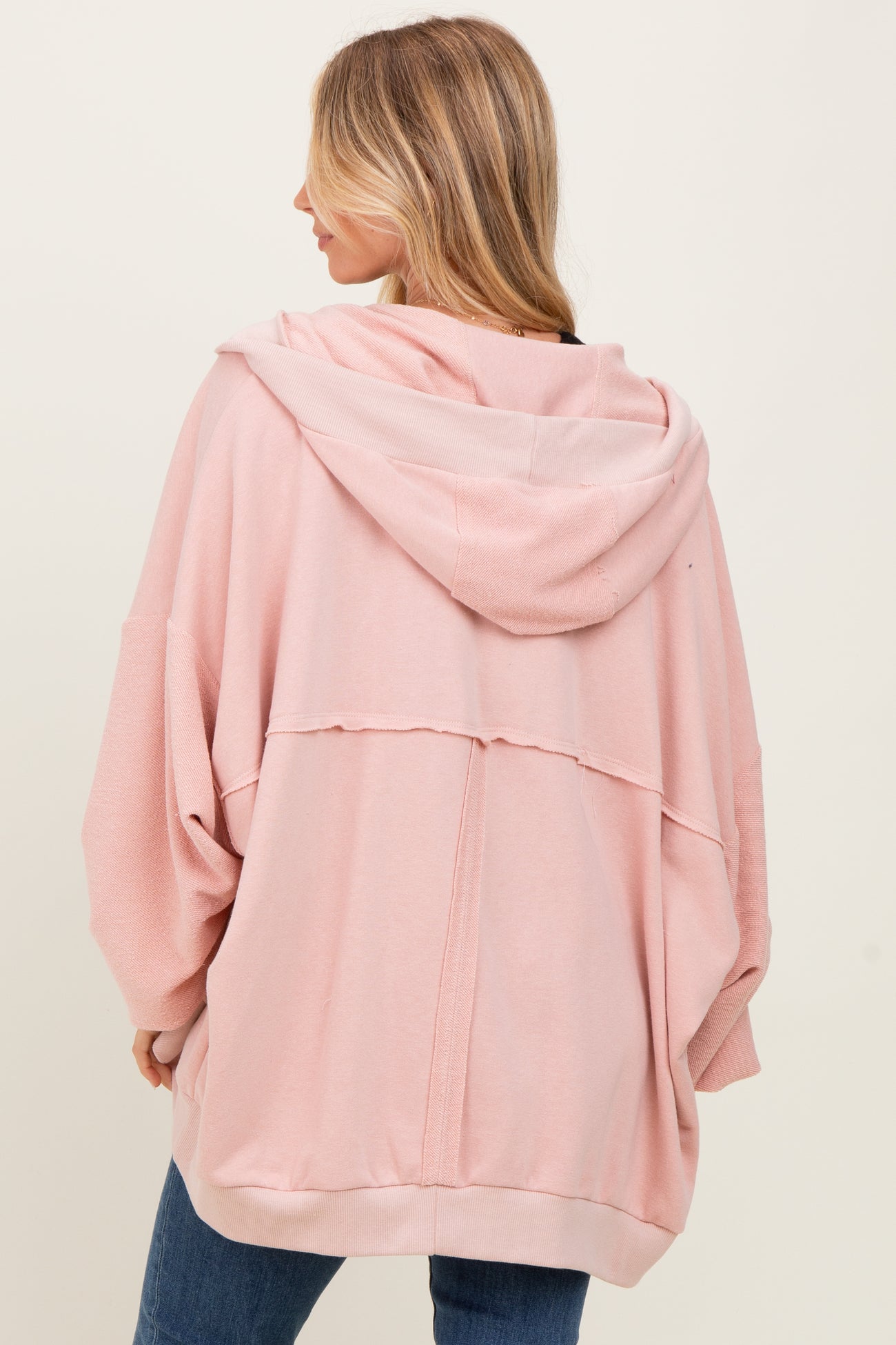 woman wearing a light pink oversized hoodie with a hood and relaxed fit, showing the back view