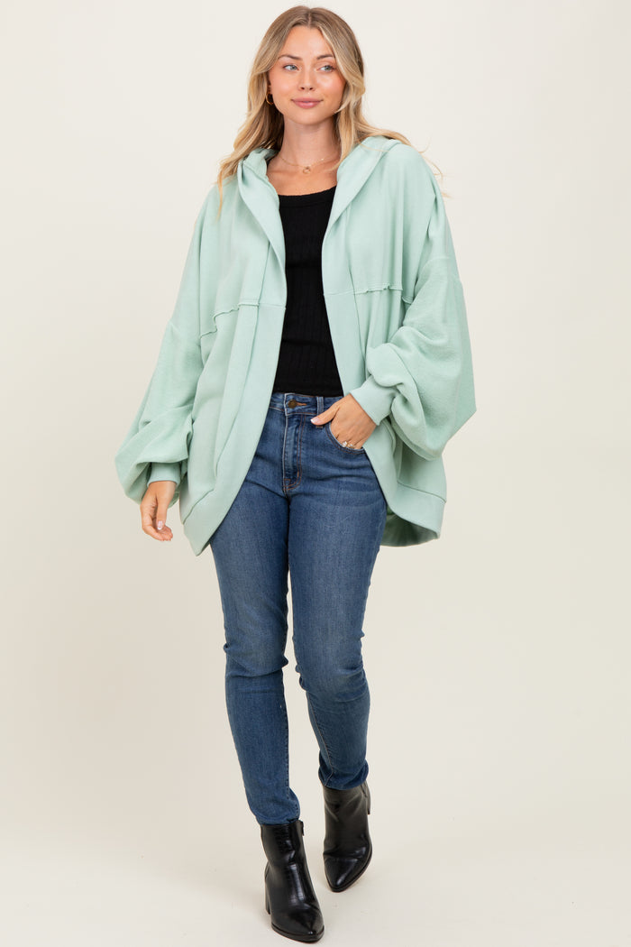 woman wearing a mint green oversized hoodie, black fitted top, and skinny jeans with ankle boots