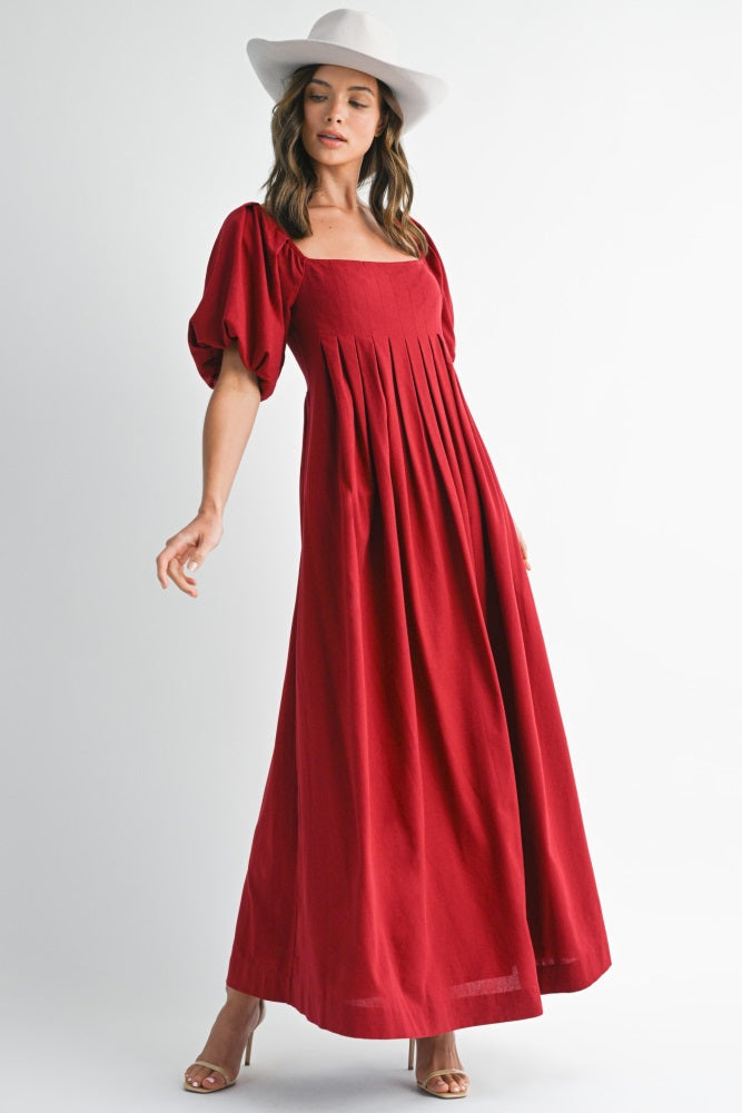 woman wearing a red maxi dress with puff sleeves and a square neckline, styled with a wide-brim hat