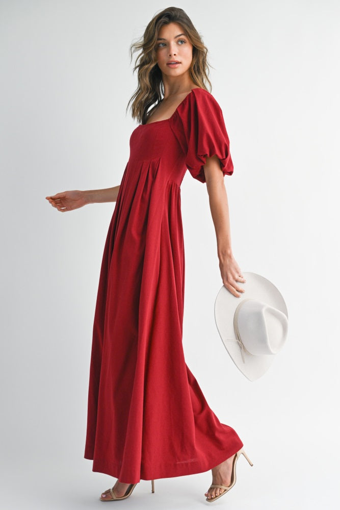 woman wearing a red maxi dress with puff sleeves and holding a wide-brimmed hat