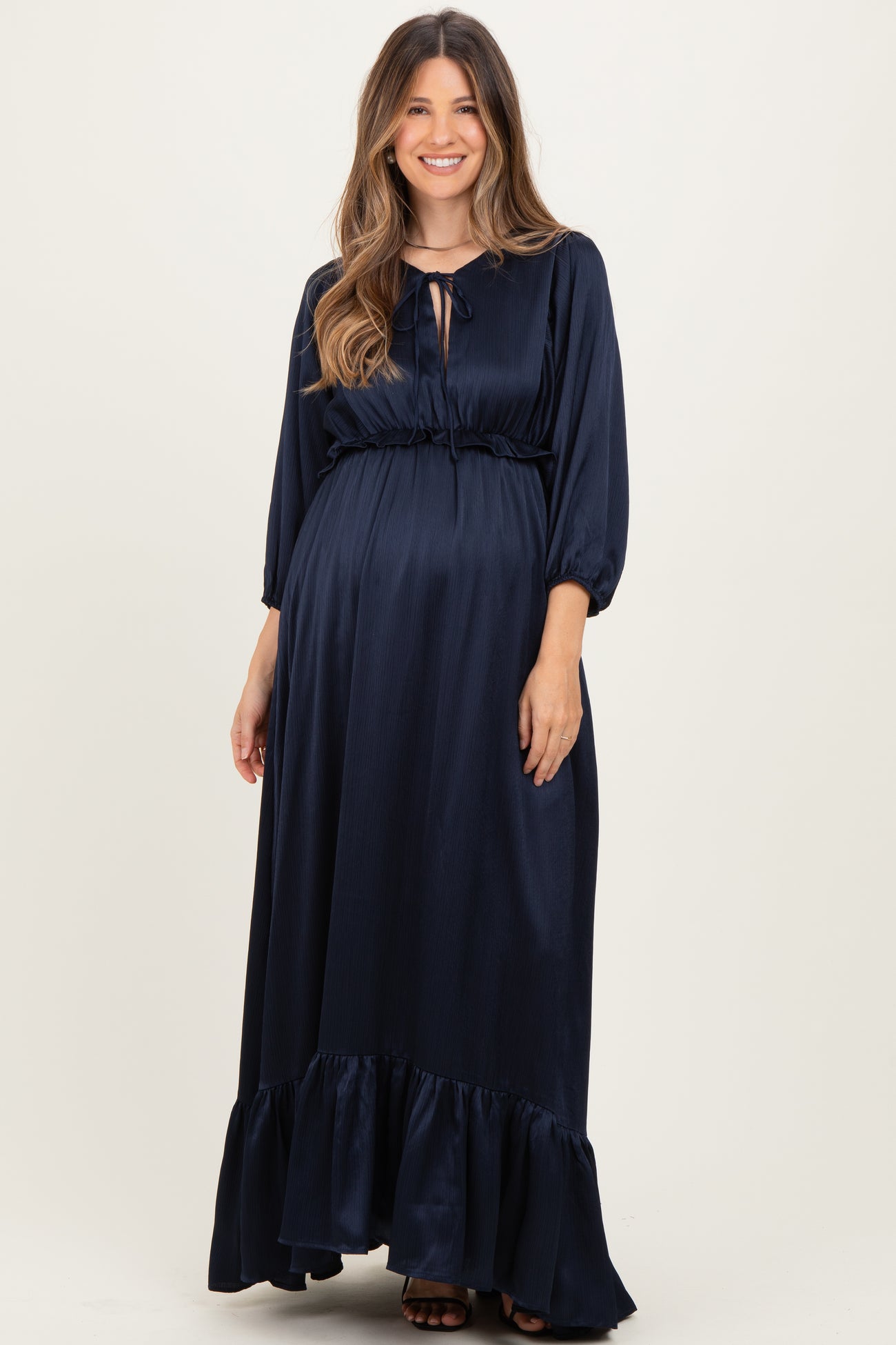 woman wearing a navy blue long sleeve maternity dress with a ruffle hem and a tied neckline, showing her baby bump