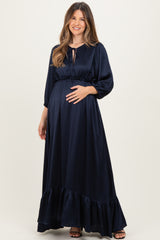woman wearing a navy blue maternity maxi dress with a tie neck and ruffled hem, cradling her baby bump