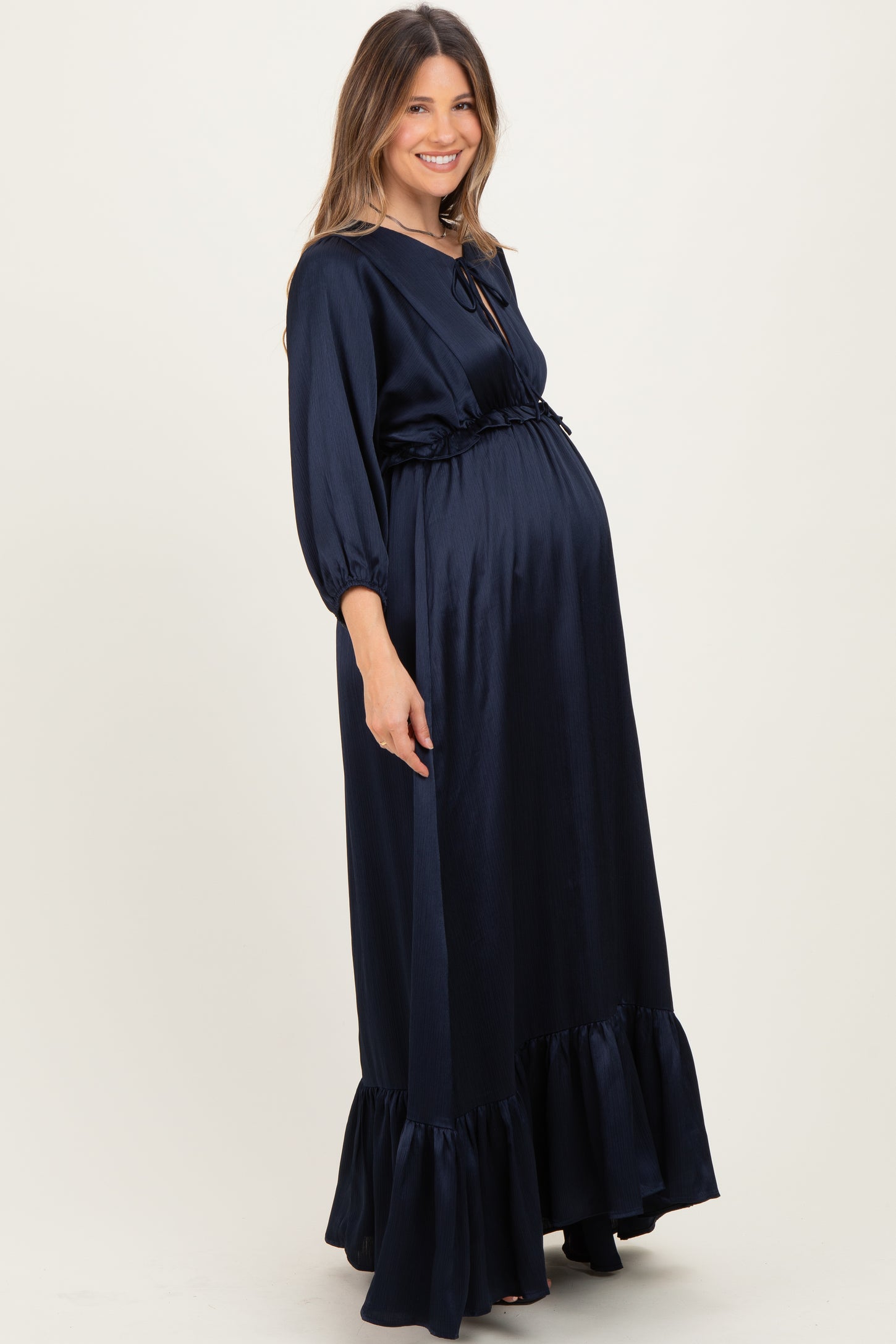 woman wearing a navy blue maternity maxi dress with ruffle hem and a tie waist, showing her baby bump