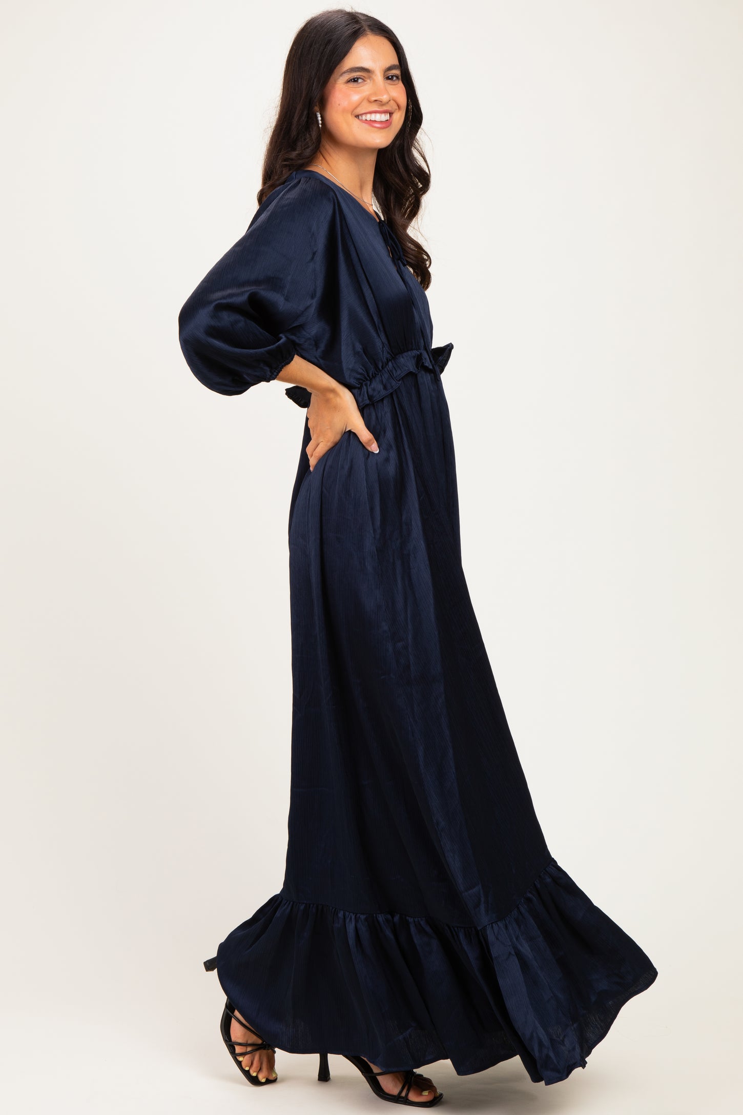 woman wearing a navy blue long sleeve maxi dress with a ruffled hem and bow detail, posing with a smile