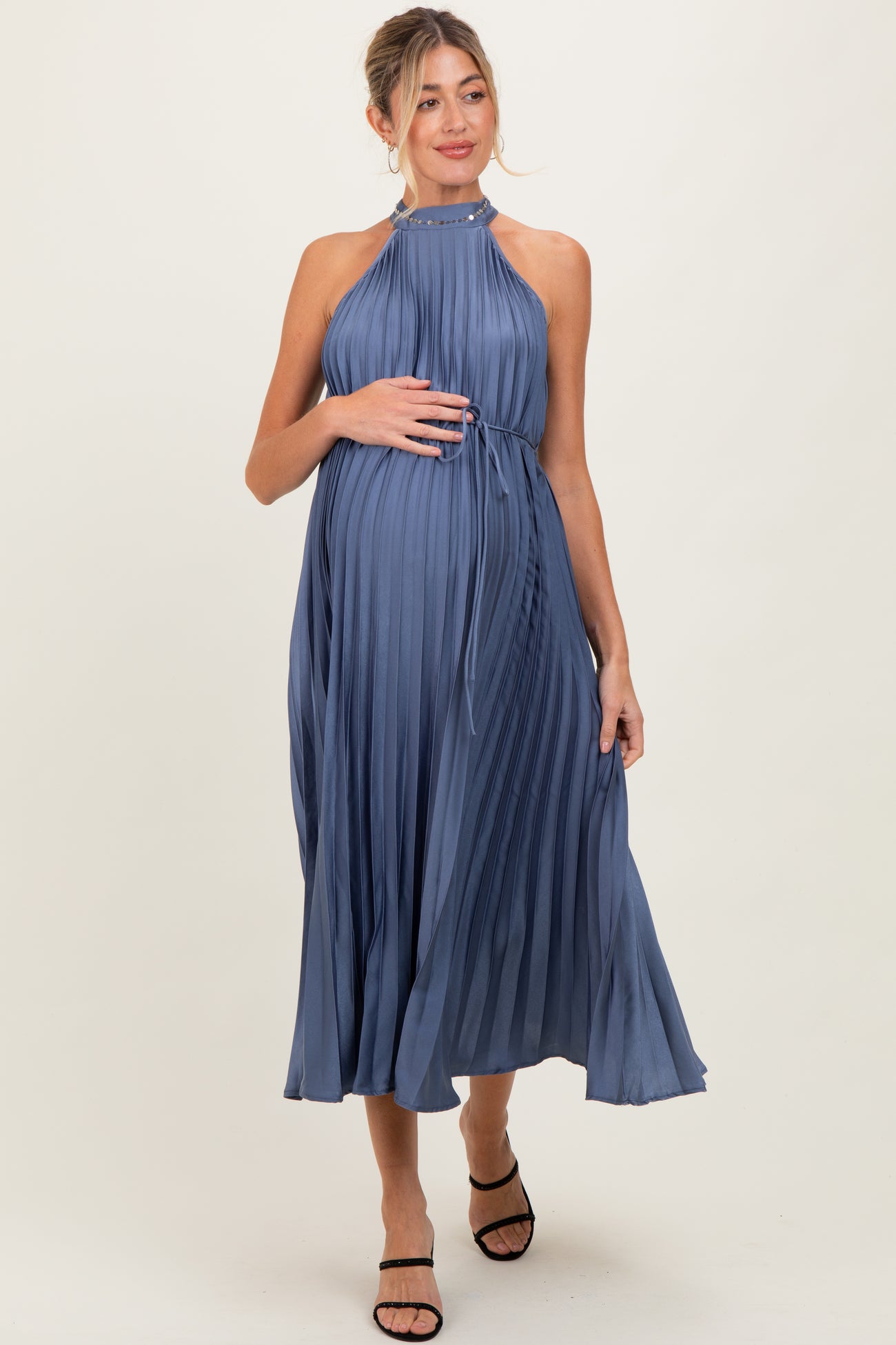 woman wearing a pleated blue maternity dress with a halter neck and a visible baby bump