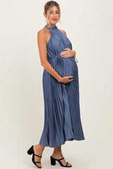 woman wearing a blue pleated maternity dress with a halter neck and holding her baby bump