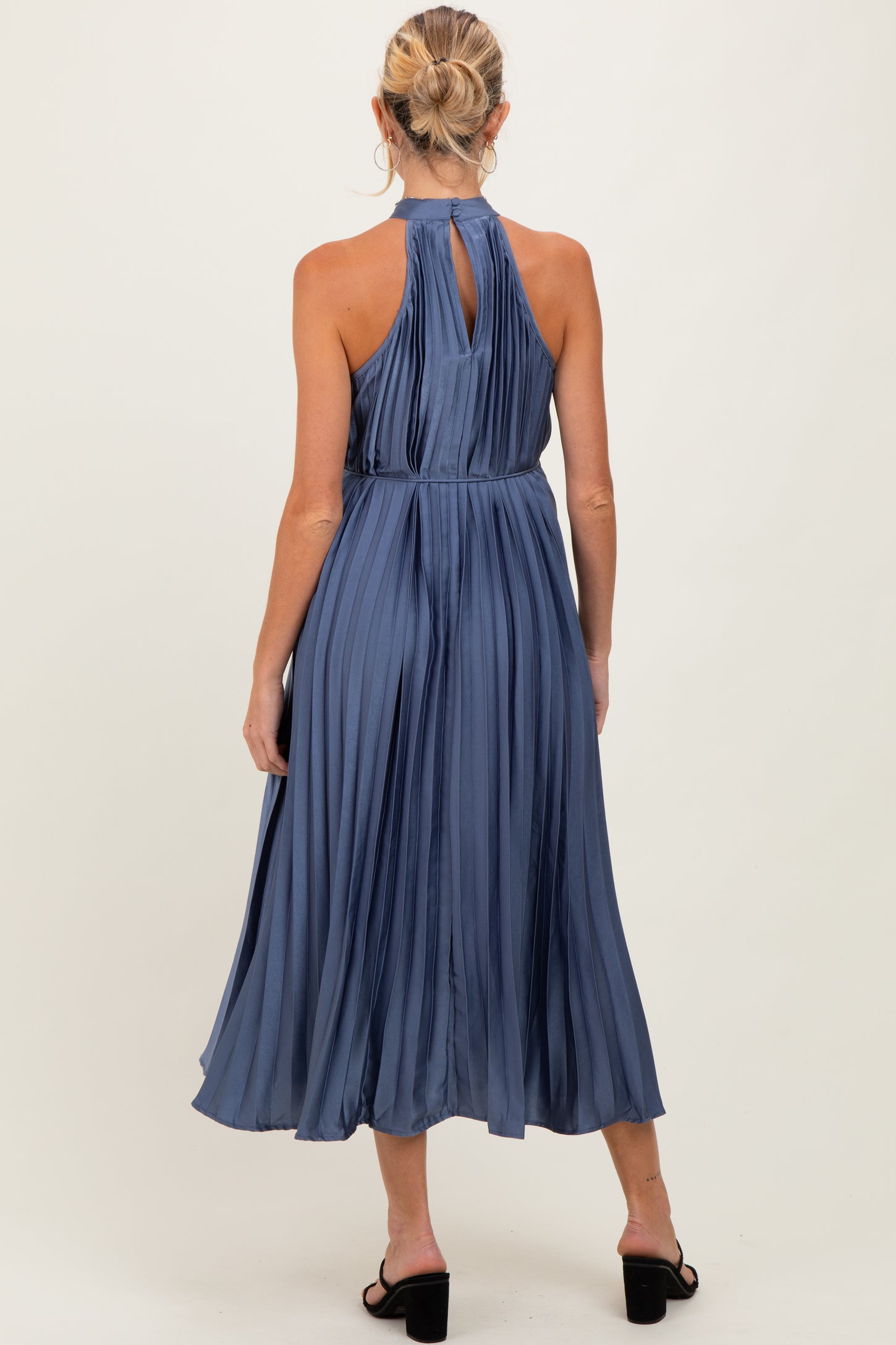 woman wearing a navy blue pleated halter maternity dress with a fitted waist and open back