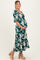 woman wearing a green floral maternity maxi dress, highlighting her baby bump while standing in side profile