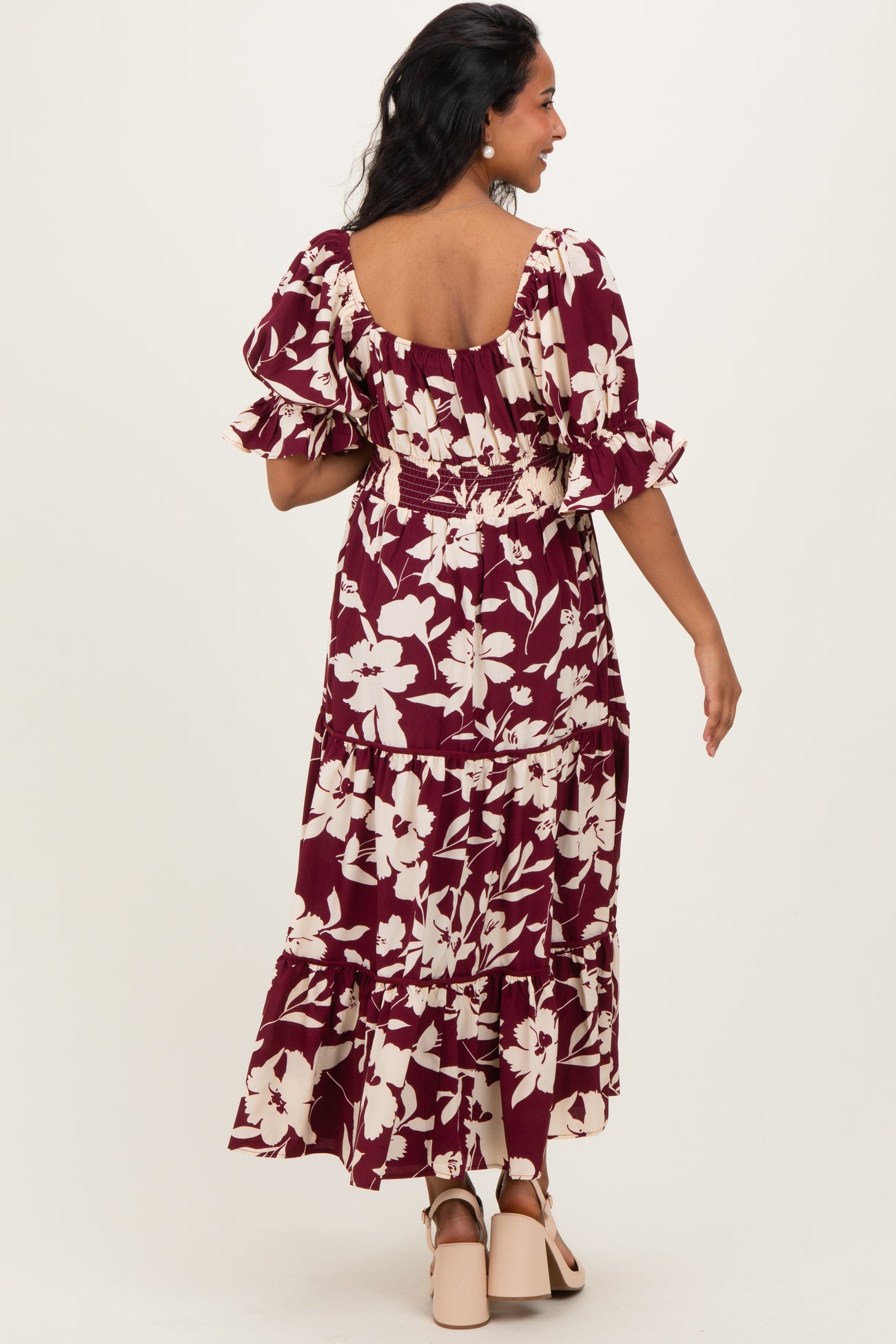 woman wearing a burgundy floral maternity maxi dress with ruffle sleeves and a tiered skirt, seen from the back