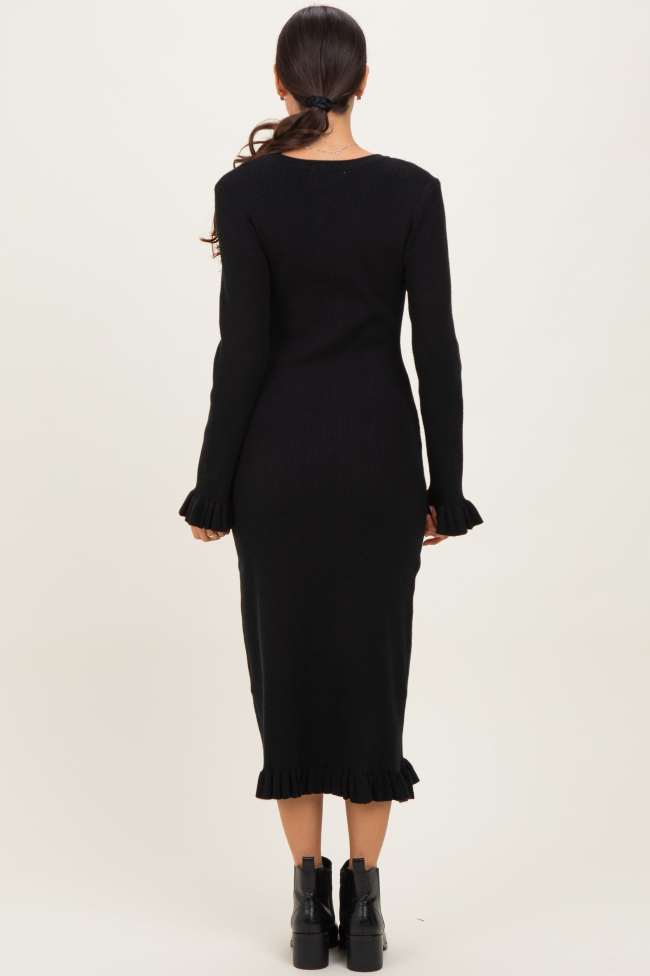 woman wearing a fitted black ribbed dress with long sleeves and ruffled hem details