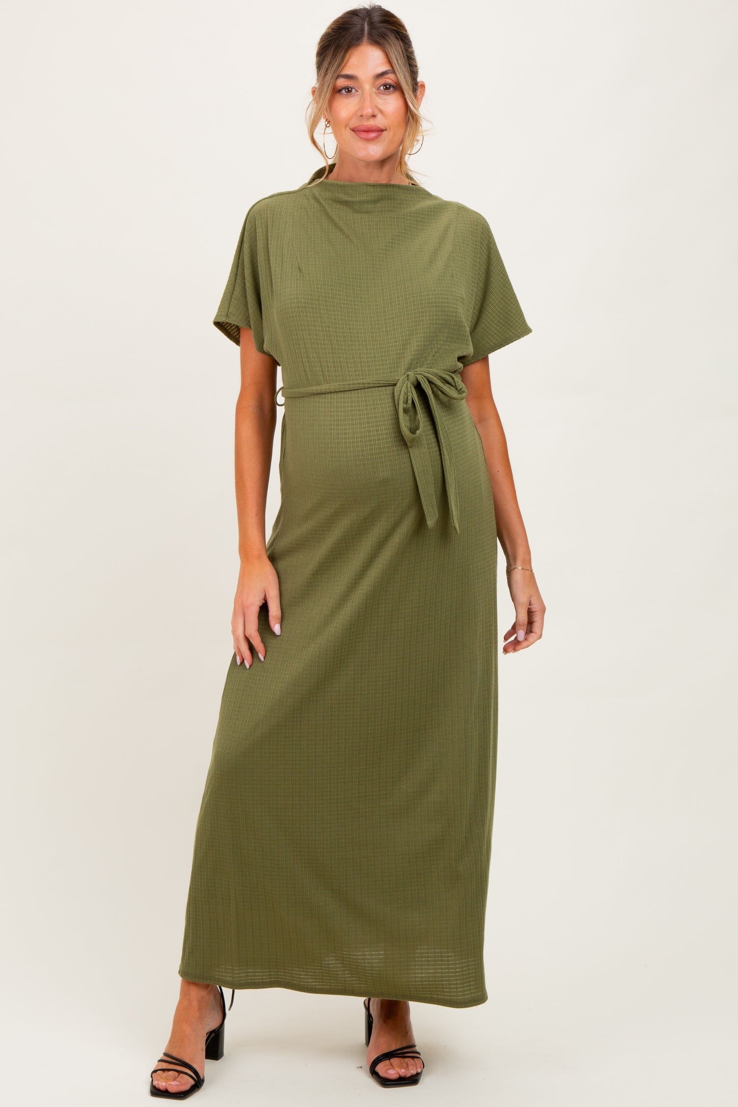 woman wearing an olive green maternity maxi dress with short sleeves and a tied waist detail, styled for a comfortable fit