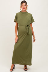 woman wearing an olive green maternity maxi dress with short sleeves and a tied waist detail, styled for a comfortable fit