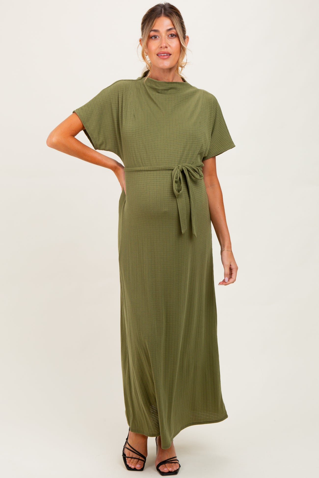 woman wearing an olive green maternity maxi dress with a tie waist and short sleeves, showing her baby bump
