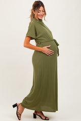 woman wearing an olive green short sleeve maternity maxi dress with a tie waist and holding her baby bump