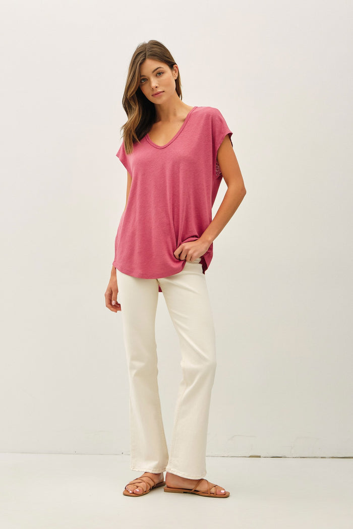 woman wearing a pink v-neck t-shirt with relaxed sleeves and white flared pants