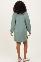 woman wearing a green ribbed long sleeve oversized dress with a high-low hem and white sandals
