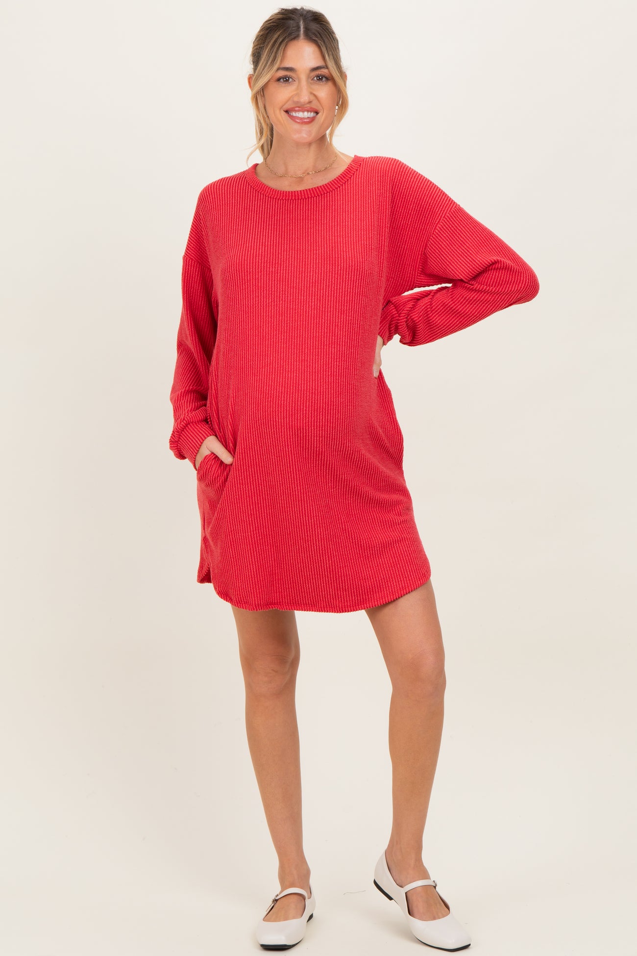 woman wearing a red ribbed maternity dress with long sleeves and pockets, featuring a visible baby bump