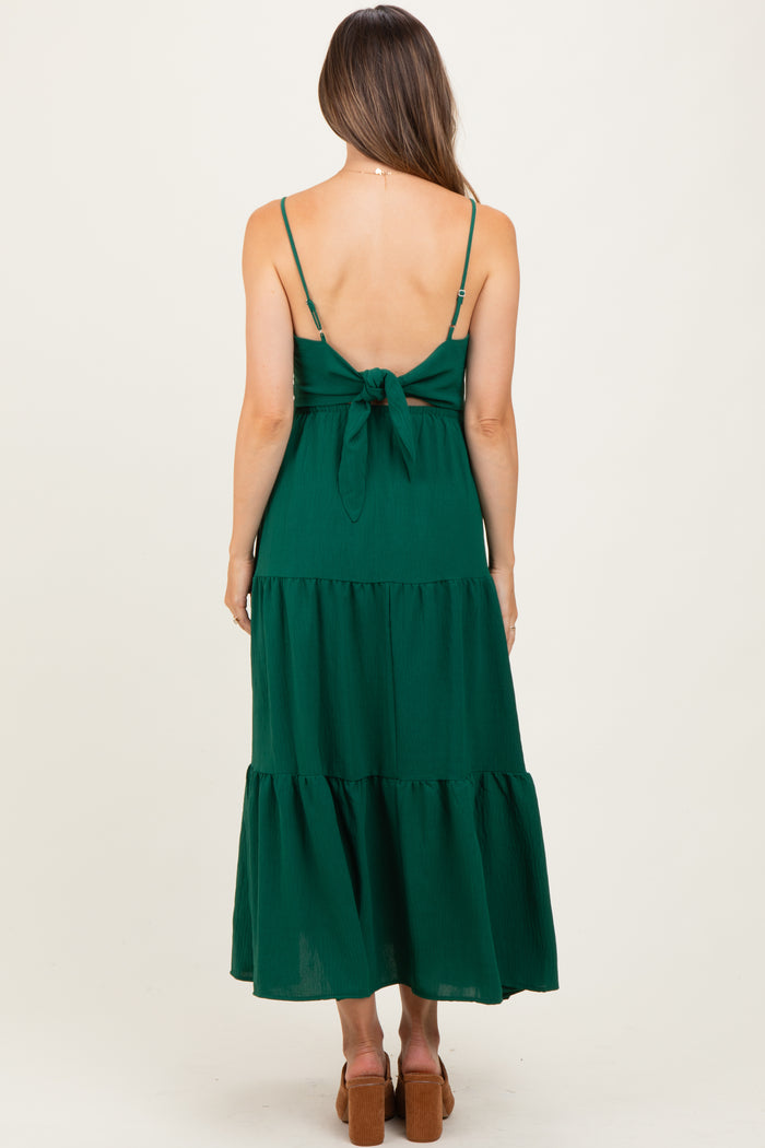 woman wearing a green maternity dress with a back tie detail and tiered skirt, showing her baby bump