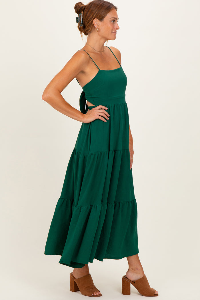 woman wearing a green tiered maxi dress with a tie back and spaghetti straps, standing sideways