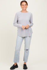 woman wearing a light gray long sleeve top with rounded hem and blue ripped jeans, standing and smiling